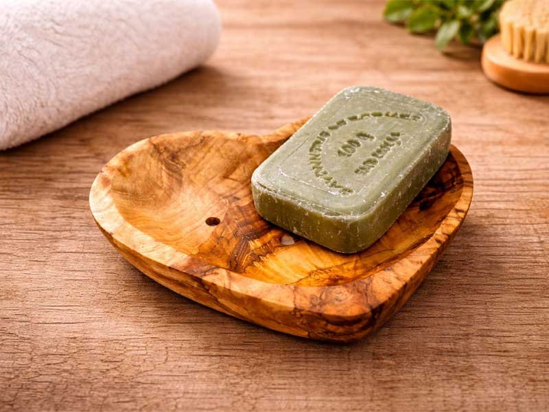 Olivenholz Seifenschale in Herzform mit Naturseife auf Holzuntergrund